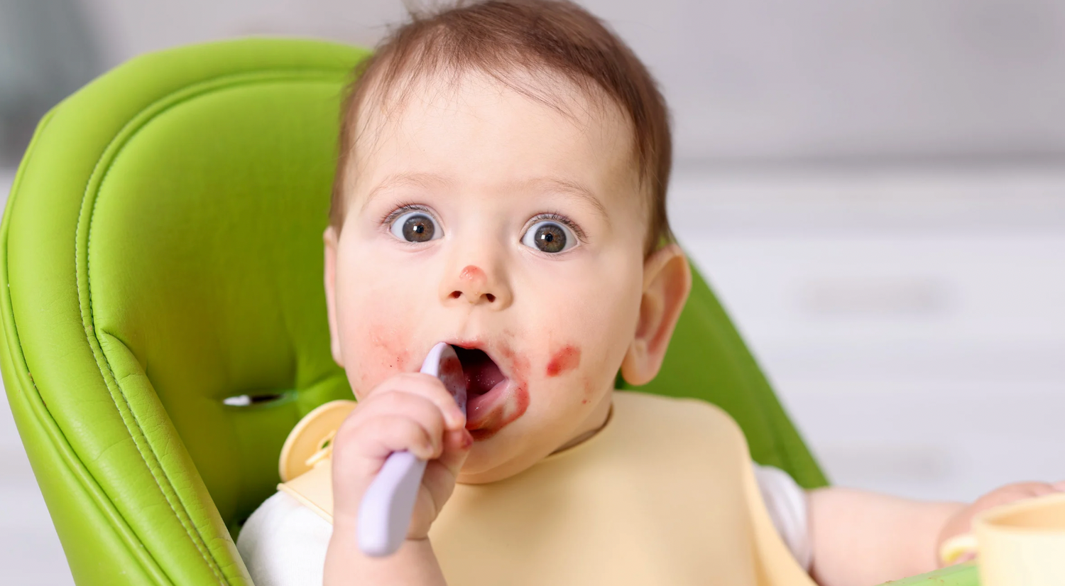 Baby practicing baby-led feeding by self-feeding with a spoon, exploring textured baby food while seated in a high chair